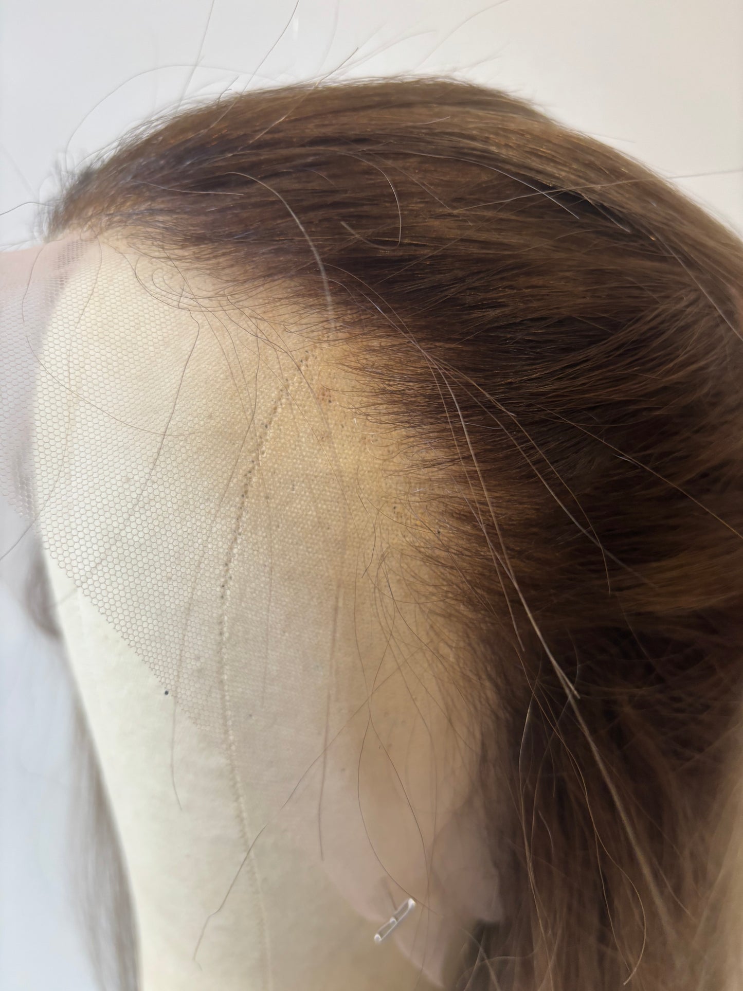 Close-up of dark brown shadow root of a wig into a medium beige blonde on a white background.